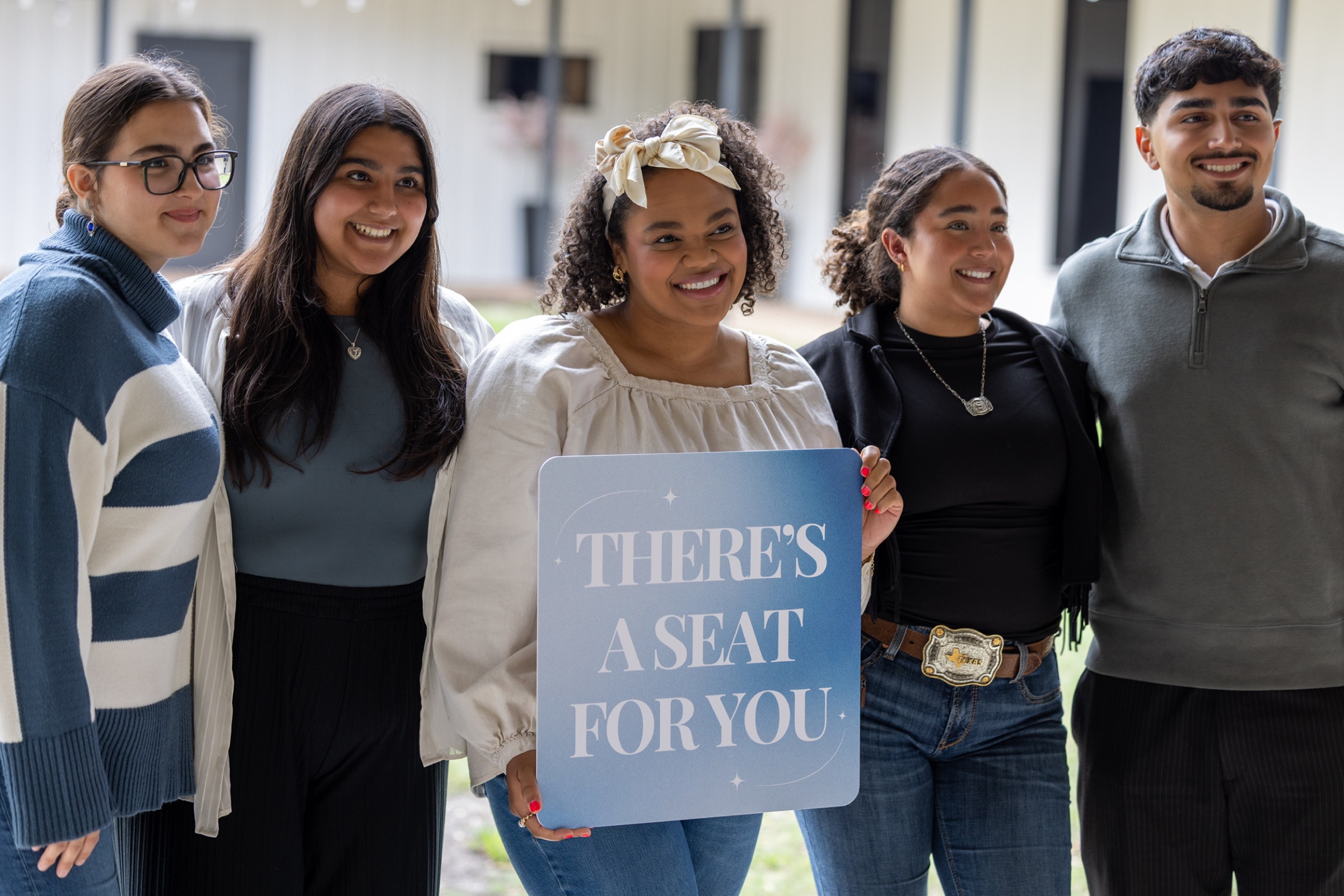 Friends outside the church holding a sign that reads: there's a seat for you